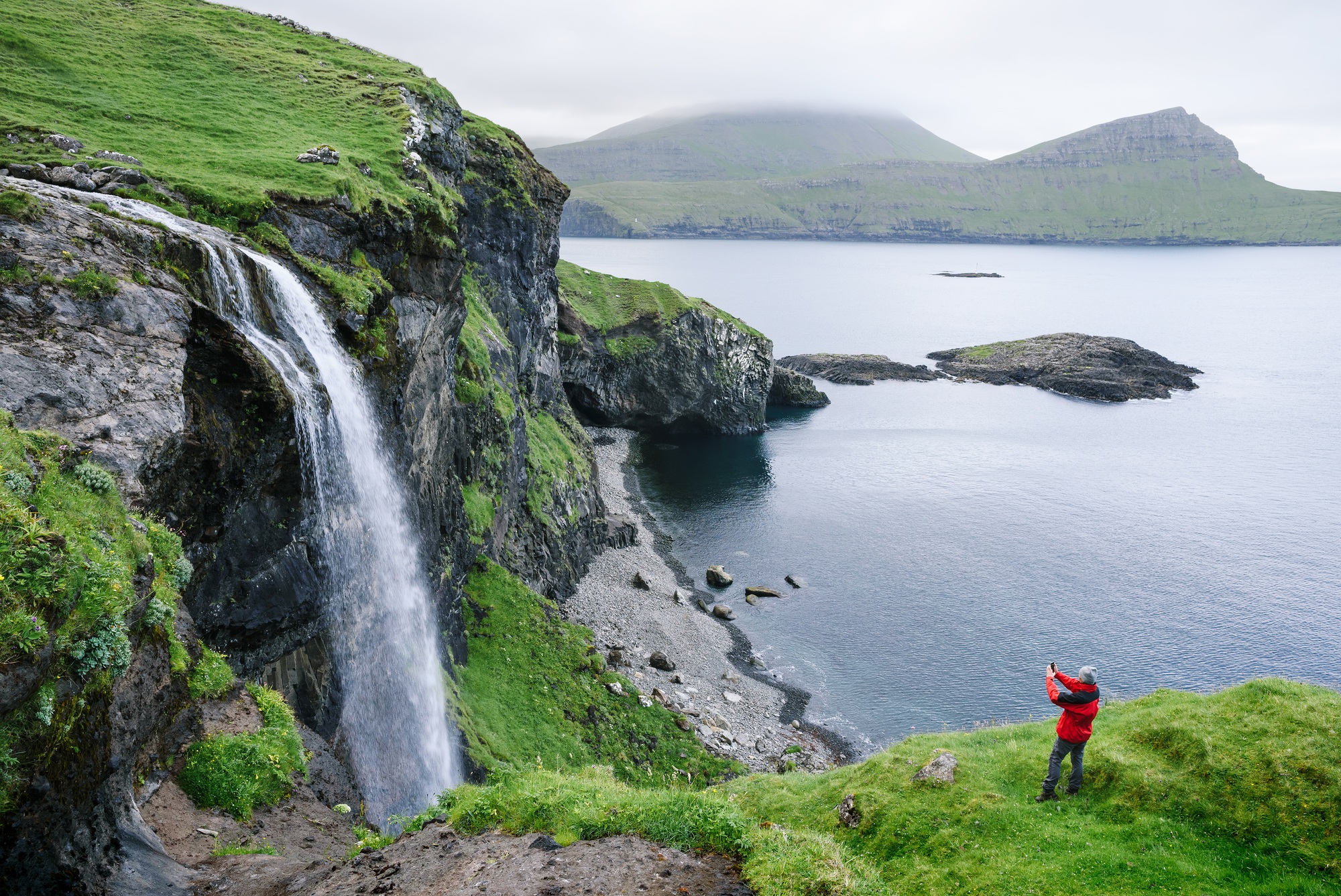 A tourist takes pictures of the Skardsafossur waterfall, Faroe Islands