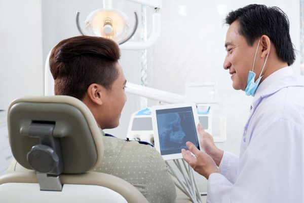 At orthodontist Smiling Asian orthodontist showing jaw x-ray to patient
